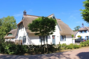 Ein traditionelles Haus mit einem Strohdach, weißen Wänden und einem kleinen Baum davor.