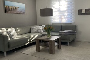 Ein modernes Wohnzimmer mit einem grauen Sofa, einem Holztisch und einem Bild an der Wand.