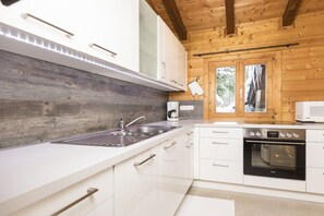 Een moderne keuken met witte kasten, een roestvrijstalen spoelbak, een inbouwoven en een raam met uitzicht op bomen.
