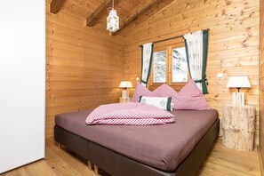 A wooden cabin bedroom with a bed, two bedside lamps, and a window with curtains.