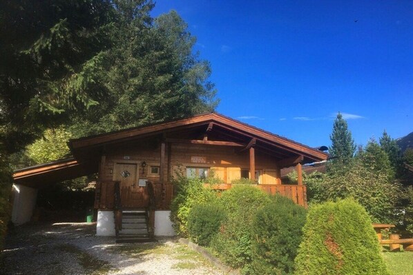 A wooden cabin with a sloped roof, surrounded by dense greenery and trees.