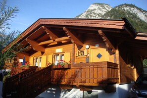 A wooden chalet with a balcony, a mountain backdrop, and a sign indicating a restaurant.