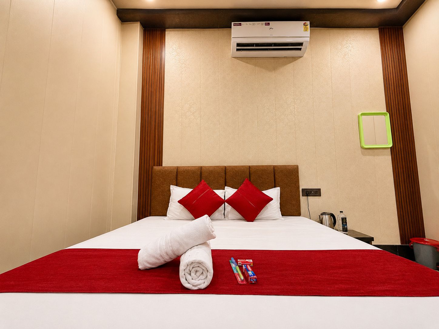 Ein Hotelzimmer mit einem Bett, einer roten Decke, einem zusammengerollten Handtuch und Toilettenartikeln auf dem Nachttisch.