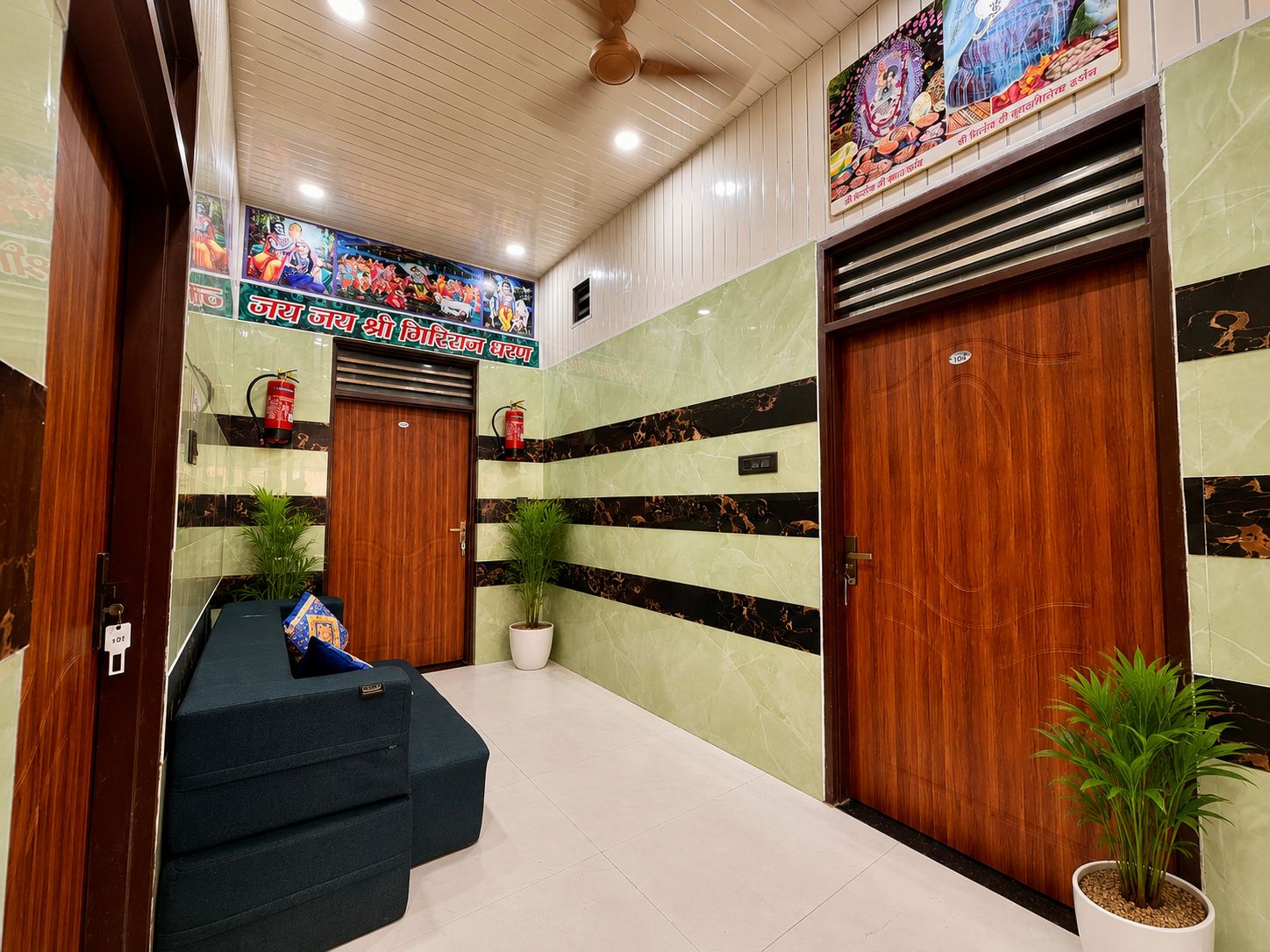Un vestíbulo de hotel con un mostrador de recepción, dos puertas de madera, un ventilador de techo y un mural en la pared.