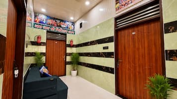 Un vestíbulo de hotel con un mostrador de recepción, dos puertas de madera, un ventilador de techo y un mural en la pared.