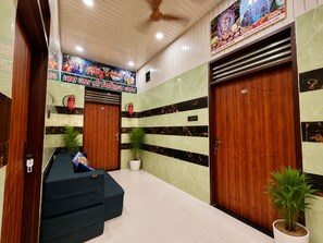 Un vestíbulo de hotel con un mostrador de recepción, dos puertas de madera, un ventilador de techo y un mural en la pared.