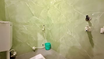 Une salle de bain avec des toilettes, un mur en marbre vert, un lavabo blanc et un seau vert.
