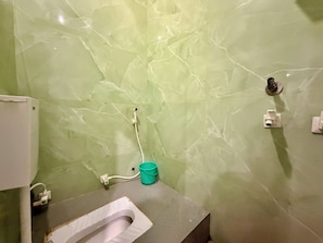 A bathroom with a toilet, a green marble wall, a white sink, and a green bucket. - Hotel JSR Inn (Mathura)