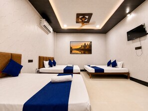 Ein Hotelzimmer mit zwei Betten, einem Deckenventilator, einer Klimaanlage, einem Flachbildfernseher und einem Bild an der Wand.