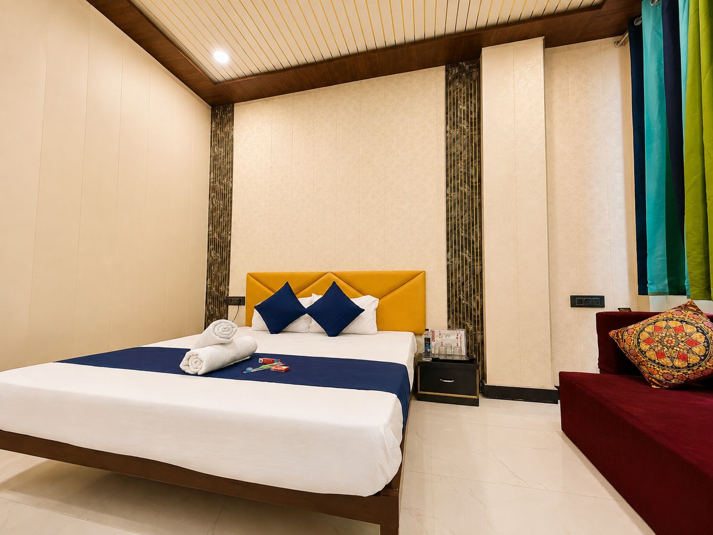 Una habitación de hotel con cama, mesita de noche, sofá rojo y ventana con cortinas.