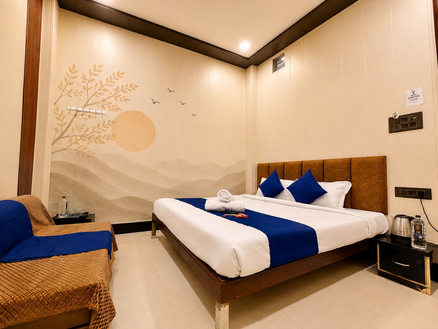 Habitación de hotel con cama, una silla, mesita de noche y un mural temático de naturaleza en la pared.