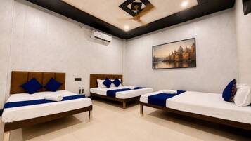 A hotel room with three single beds, a ceiling fan, an air conditioning unit, and a large window with a cityscape view.