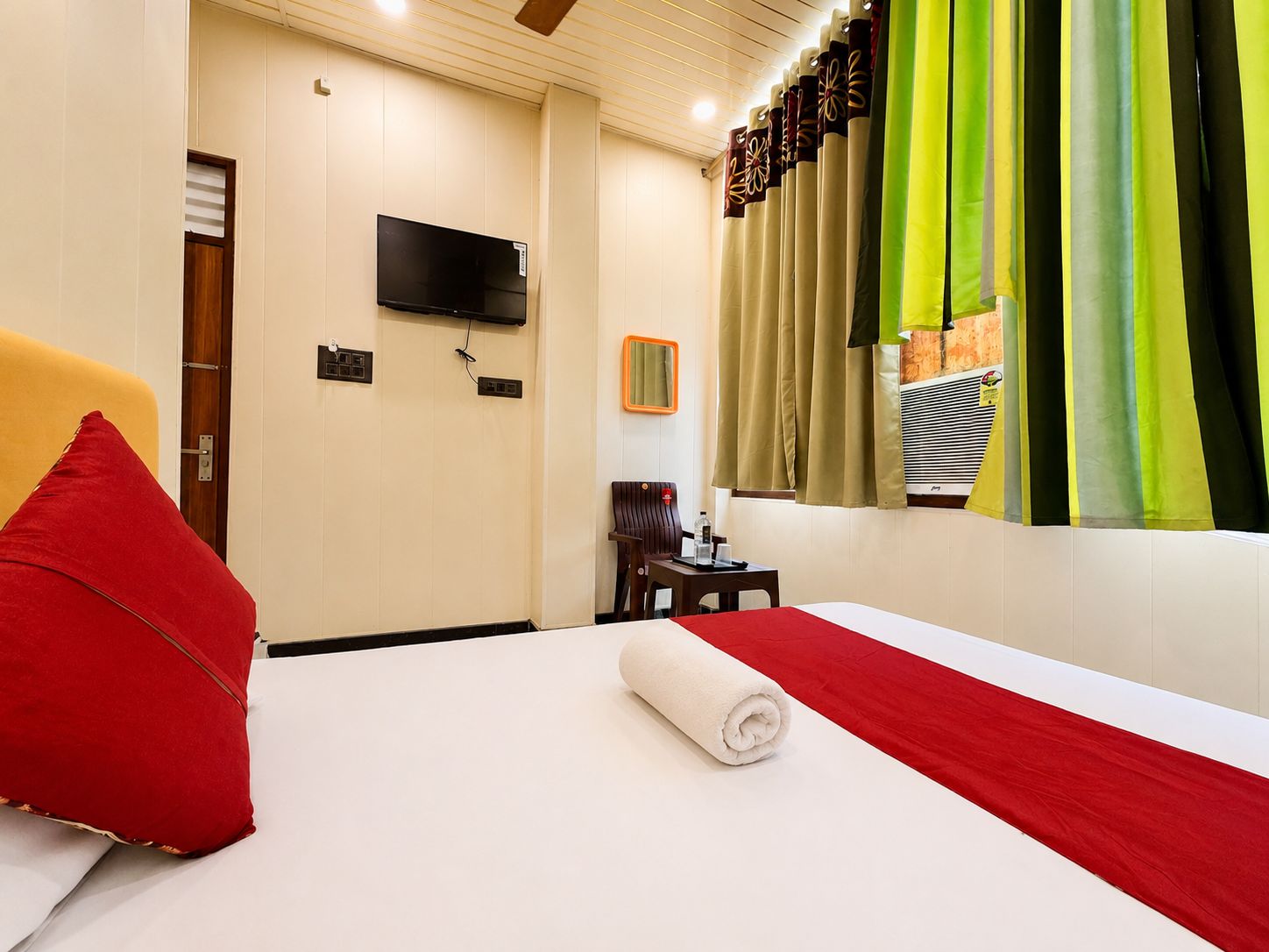 Una habitación de hotel con cama, televisión, sillón, mesita y espejo.