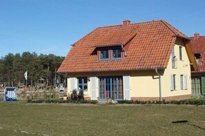 A two-story house with a red-tiled roof, a small porch with a table and chairs, and a flag in the background. - Holiday home in Glowe with swimming pool (Glowe)