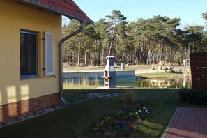 A yellow building with a window and a door, a small pond, and a wooden fence. - Holiday home in Glowe with swimming pool (Glowe)