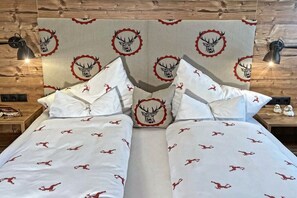 A double bed with a patterned bedspread and matching pillows, set against a wooden headboard with a deer motif. - Tyrolean charm in the Stubai Valley - NEW! (Telfes im Stubai)