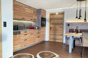 A modern kitchen with wooden cabinetry and a dining area with a table and chairs. - Tyrolean charm in the Stubai Valley - NEW! (Telfes im Stubai)