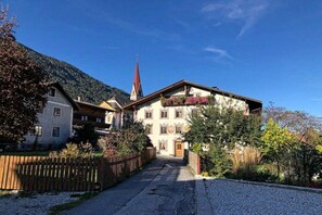 A traditional Alpine-style building with a steeply pitched roof, a visible church steeple, and a gravel driveway leading to the entrance. - Tyrolean charm in the Stubai Valley - NEW! (Telfes im Stubai)