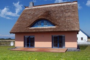 A house with a thatched roof, two large windows, and a wooden deck. - Holiday home in Lancken with swimming pool (Lancken)
