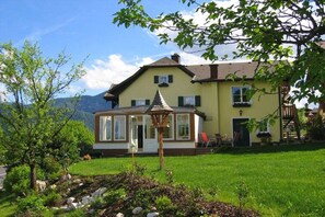 A two-story house with a conservatory, a garden with a small tree, and a mountain in the background. - Holiday apartment with 1 bedroom (Unterach am Attersee)