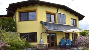 A two-story house with a yellow facade, large windows, and a covered patio with outdoor furniture. - Holiday apartment in Waren with swimming pool (Waren)