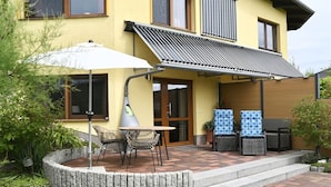 A yellow building with a covered patio area, outdoor seating, and a small garden. - Holiday apartment in Waren with swimming pool (Waren)