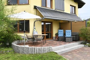 Un edificio amarillo con un patio cubierto, mesas al aire libre y un pequeño jardín.