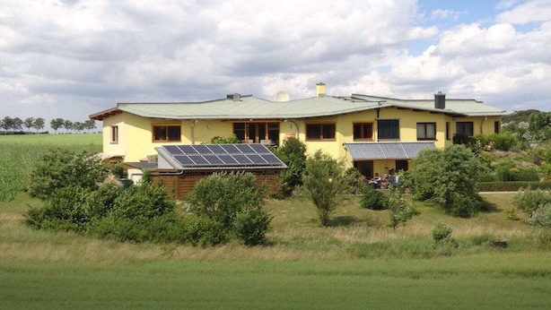 A two-story house with a green roof, surrounded by greenery and a field. - Holiday apartment in Waren with swimming pool (Waren)