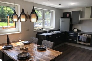 A modern kitchen with a dining area, featuring a wooden table, black plates, and hanging pendant lights. - Holiday apartment family Glanznig (Werfen)