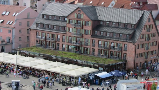 A multi-story building with a green roof, surrounded by a bustling outdoor market area with various stalls and people. - Holiday apartment in Waren with swimming pool (Waren)