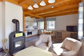 Ein gemütliches Wohnzimmer mit Kamin, Holzbalkendecke und einer Essecke mit Tisch und Stühlen.