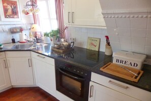 A kitchen with white cabinets, a black countertop, a stove, and a bread box. - Old Doctor's House 2 (Juist)