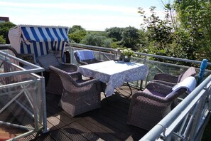 An outdoor deck with wicker furniture, a table with a white tablecloth, and a striped awning. - Old Doctor's House 2 (Juist)