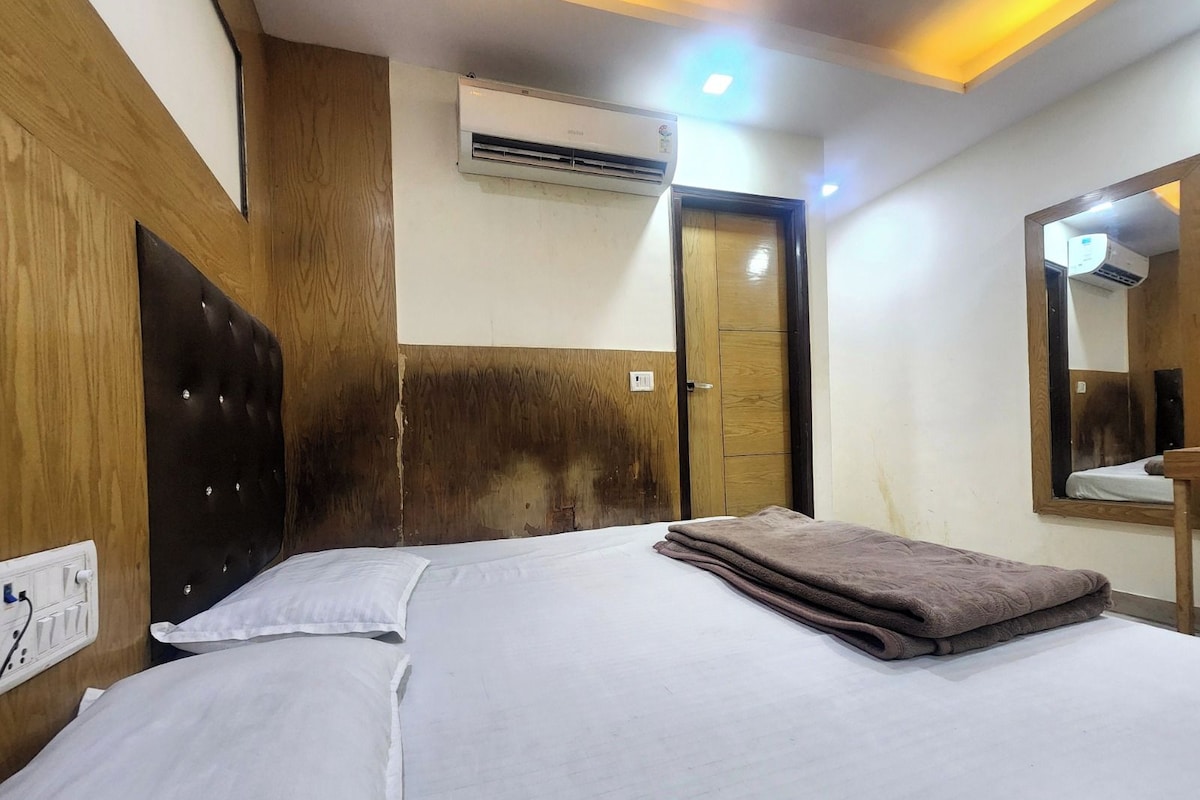 A hotel room with a bed, a wooden headboard, an air conditioning unit, a door, and a mirror.
