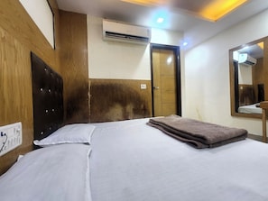 A hotel room with a bed, a wooden headboard, an air conditioning unit, a door, and a mirror. - Oly Hotel Cottage lord Krishna  (New Delhi)