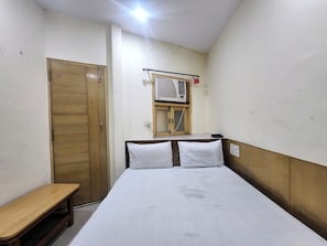 A room with a bed, a wooden wardrobe, a bench, and an air conditioning unit mounted on the wall. - Oly Hotel Cottage lord Krishna  (New Delhi)