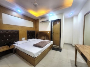A bedroom with a bed, bedside tables, a wooden headboard, an air conditioning unit, and a door. - Oly Hotel Cottage lord Krishna  (New Delhi)
