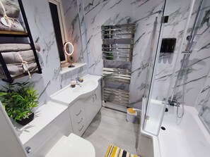 Une salle de bain moderne avec un pare-baignoire en marbre, un meuble-lavabo avec un miroir, une douche en verre et des toilettes.