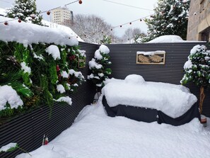 Un espacio exterior cubierto de nieve, con un muro de metal negro, un cartel de bienvenida y un banco nevado.