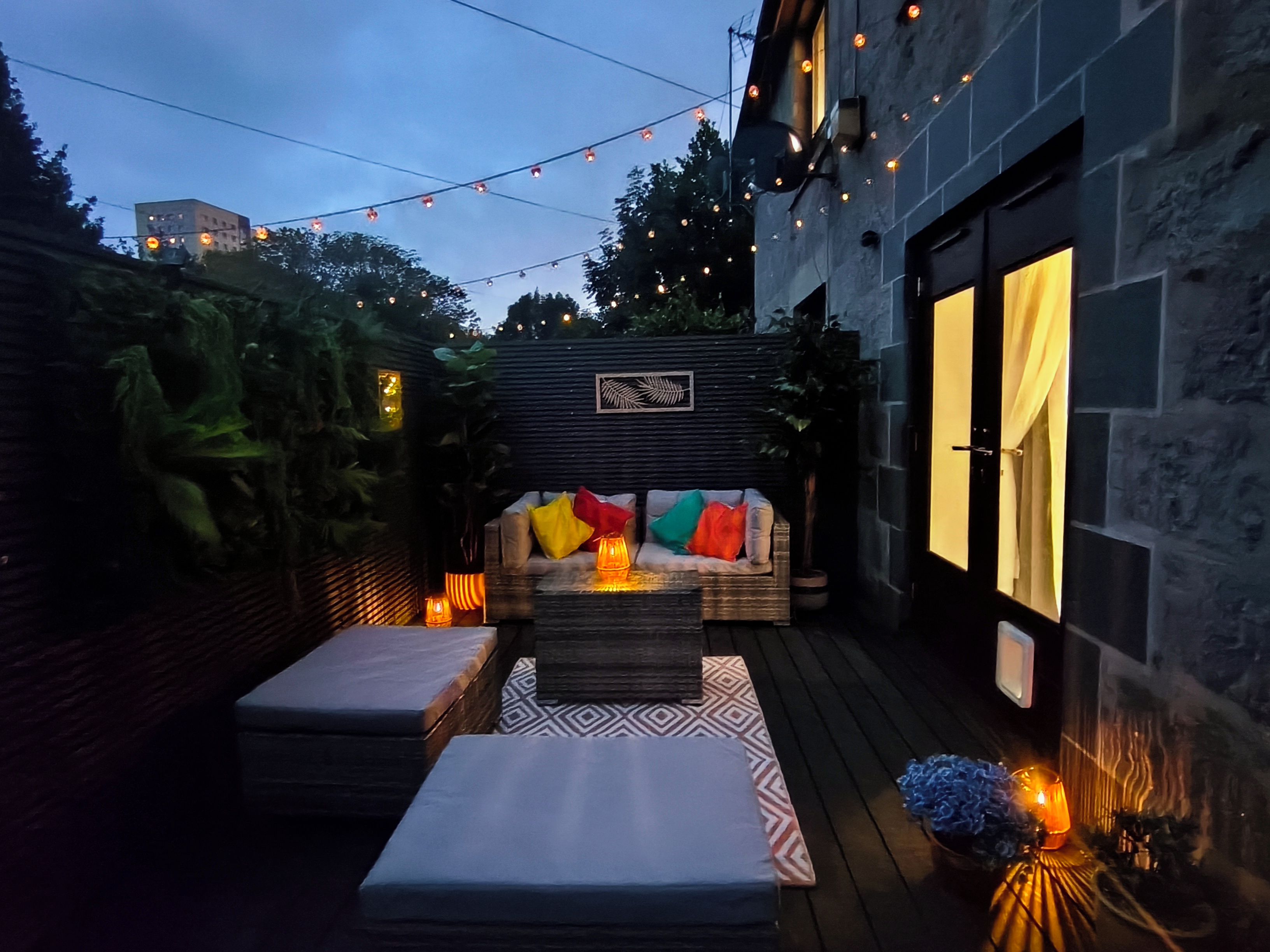 An outdoor patio area with a sofa, cushions, and a patterned rug.