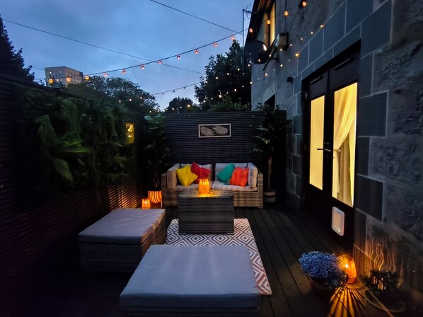 Un espace extérieur aménagé en terrasse, avec un canapé, des coussins et un tapis à motifs.