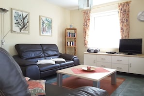 A living room with a black leather sofa, a wooden bookshelf, a television, and a window with curtains. - in the beech park W 1 (Ostseebad Prerow)