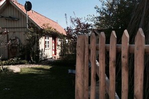 Ein Holzzaun mit einem Tor, eine rote Tür und ein Haus mit rotem Dach und weißen Wänden.
