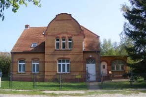 Ein zweistöckiges Backsteingebäude mit Satteldach, einer kleinen Veranda und einem umzäunten Garten.