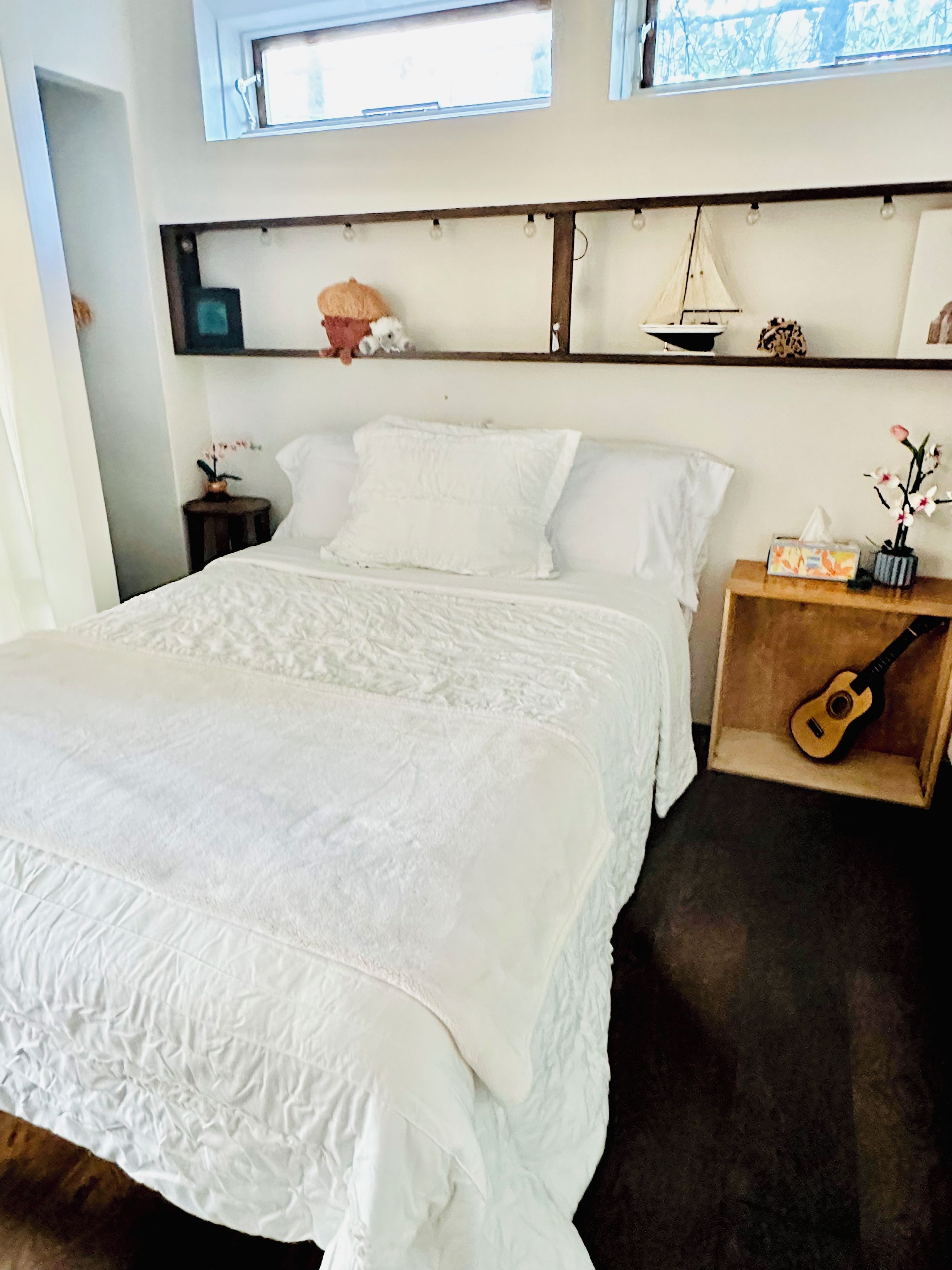Una camera da letto con un letto, un comodino, una chitarra e uno scaffale con oggetti decorativi.