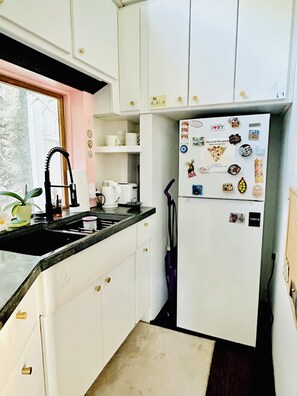 Una cucina compatta con mobili bianchi, un piano di lavoro nero, un lavello in acciaio inossidabile e un frigorifero decorato con diversi magneti e bigliettini.