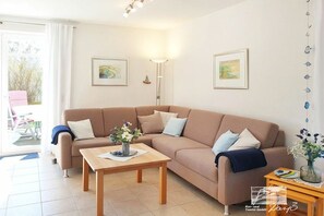 Ein Wohnzimmer mit einem beigefarbenen Sofa, einem Holztisch und zwei gerahmten Kunstwerken an der Wand.