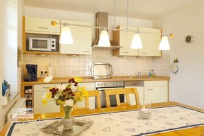 Eine Küche mit Mikrowelle, Toaster und Geschirrspüler, einem Esstisch mit Blumenvase und Pendelleuchten.