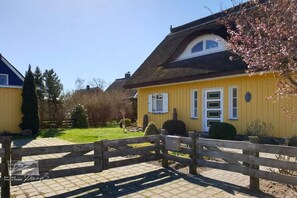 Ein gelbes Gebäude mit einem Strohdach, einem Holzzaun und einem gepflegten Garten.