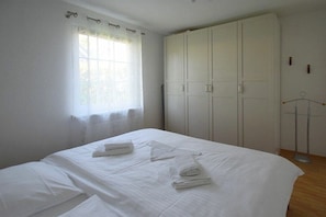 A bedroom with a bed, a wardrobe, and a window with curtains. - Buchengrund W 2 || Ostseebad Prerow (Ostseebad Prerow)